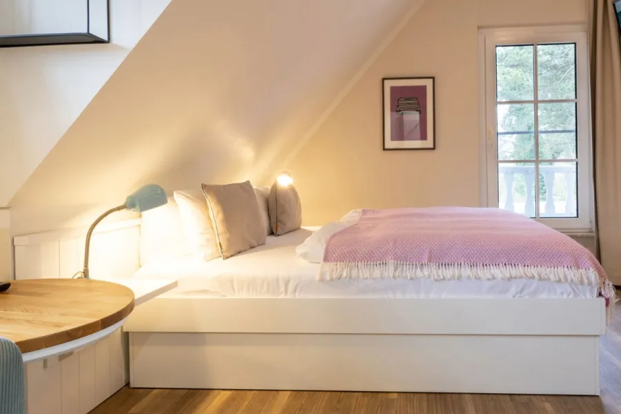 Doppelzimmer Petit im STRANDHAUS Ahrenshoop mit rosafarbener Decke, Dachschräge und warmem Licht.
