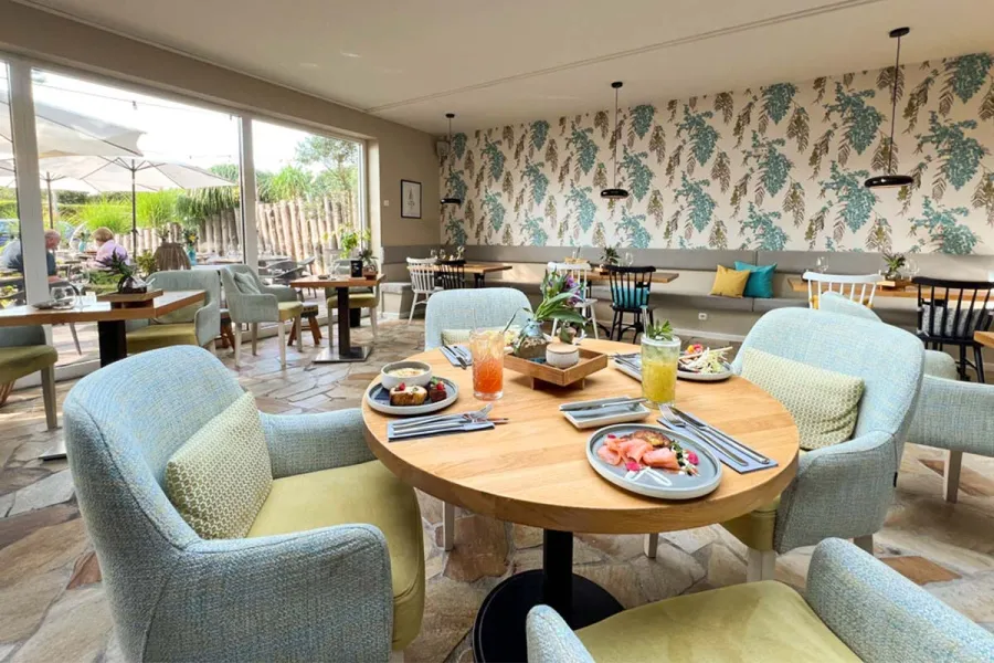 Heller Restaurantbereich der ZIMTZIEGE im STRANDHAUS Ahrenshoop mit gedeckten Tischen, Sesseln und Blick auf die Terrasse.