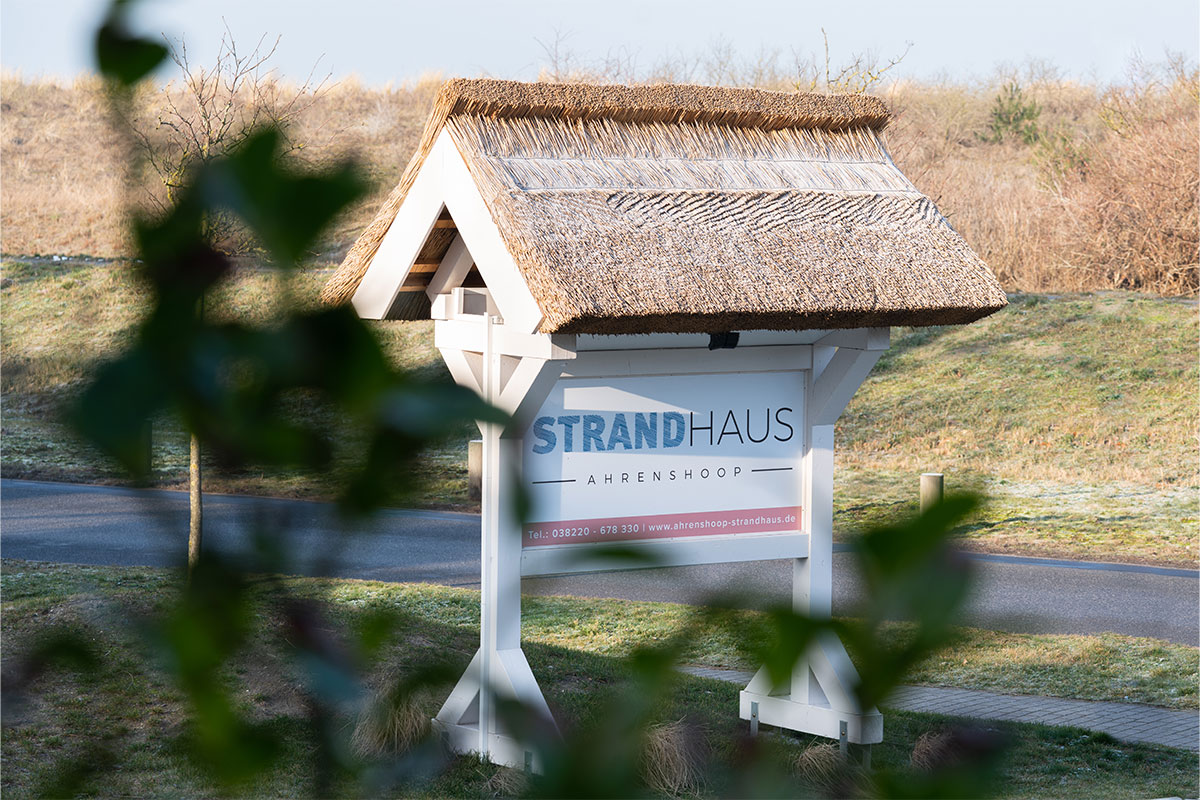 Eingangsschild mit Reetdach und Schriftzug STRANDHAUS Ahrenshoop in der Dünenlandschaft.