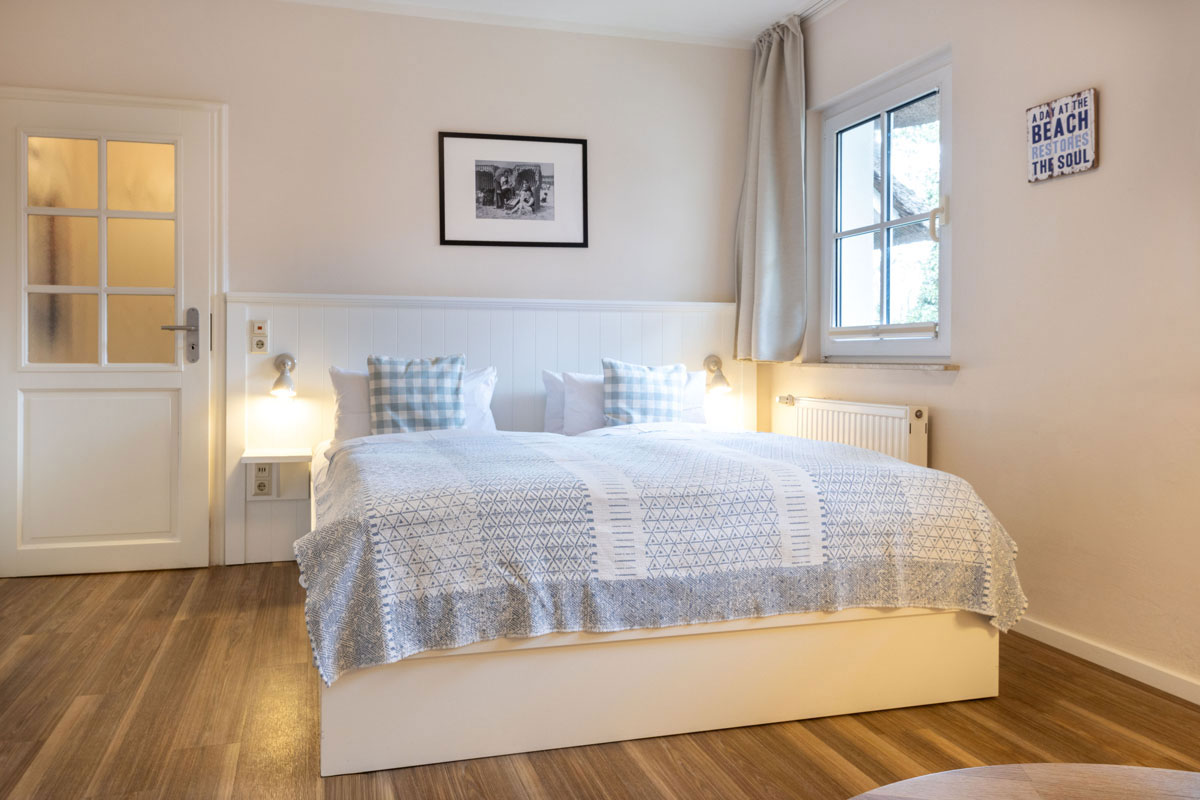 Doppelbett im Doppelzimmer Petit des STRANDHAUS Ahrenshoop mit blau-weißen Kissen und warmem Wandlicht.