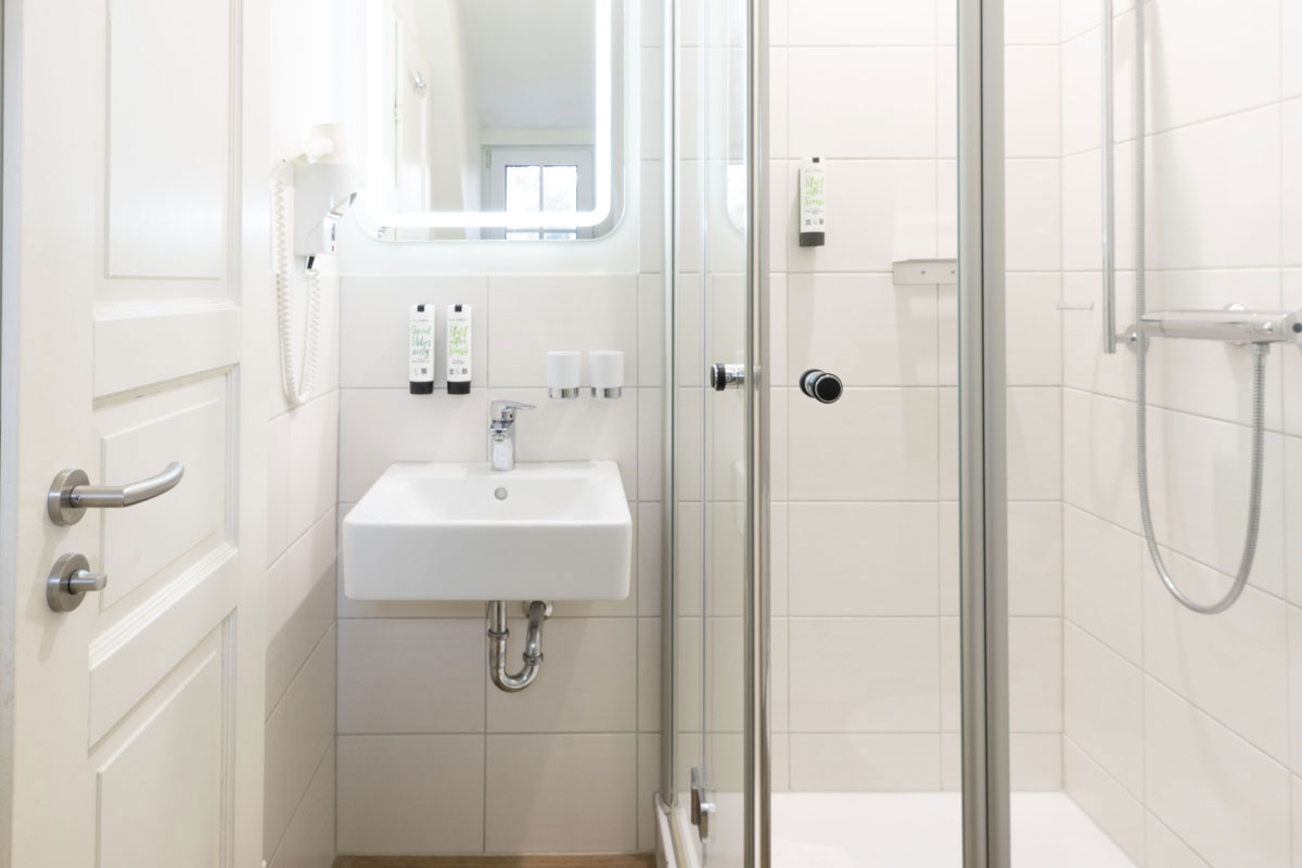 Duschbad im Doppelzimmer Petit des STRANDHAUS Ahrenshoop mit Glasdusche, Waschbecken und beleuchtetem Spiegel.