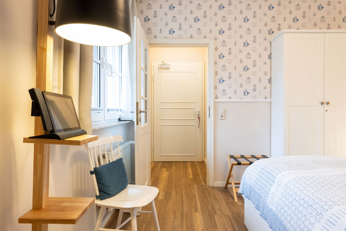 Doppelzimmer Petit im STRANDHAUS Ahrenshoop mit Schreibplatz, gemusterter Tapete und weißem Kleiderschrank.