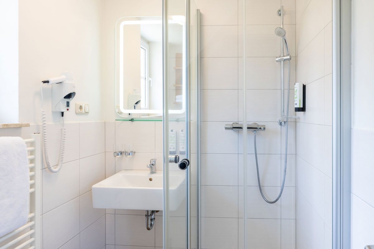 Helles Bad im STRANDHAUS Ahrenshoop mit Dusche, Waschbecken, beleuchtetem Spiegel und Haartrockner.