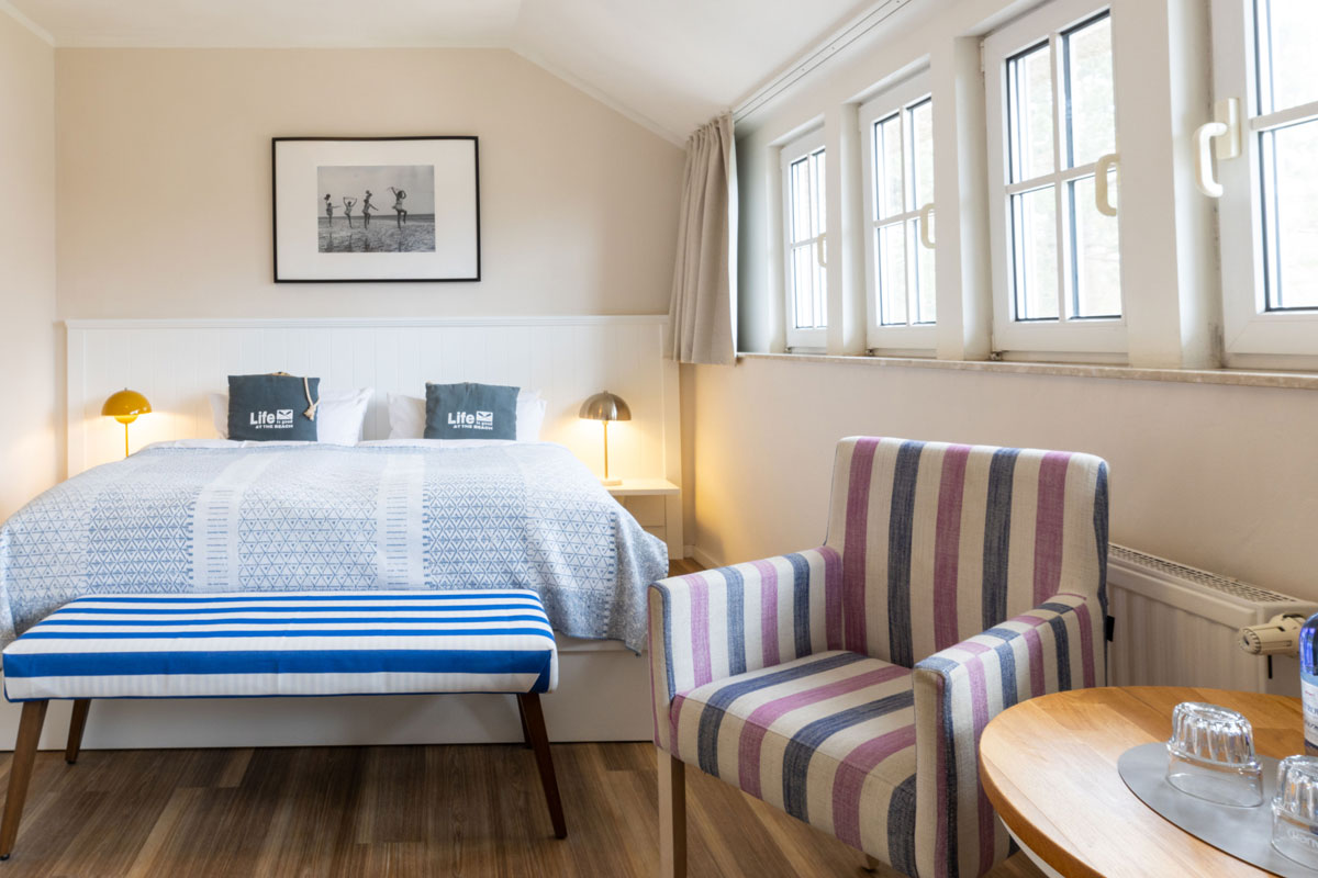 Doppelzimmer im STRANDHAUS Ahrenshoop mit Doppelbett, Sessel, Bettbank und großen Fenstern.