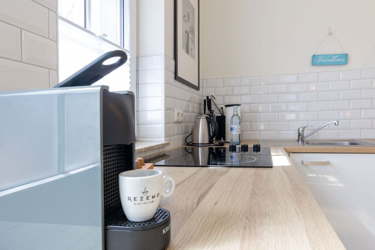 Küchenzeile im Apartment des STRANDHAUS Ahrenshoop mit Kaffeemaschine, Kochfeld, Wasserkocher und Holzarbeitsplatte.