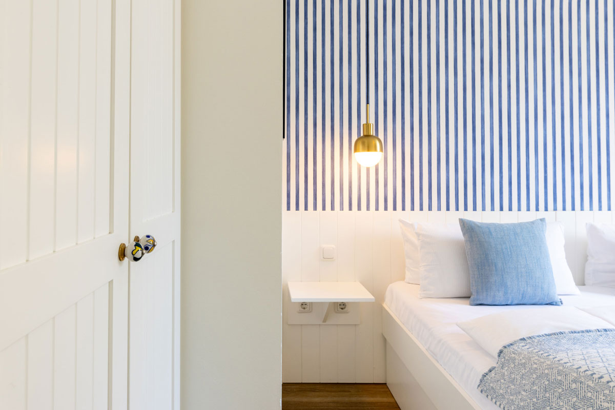 Blick ins Schlafzimmer des Apartments im STRANDHAUS Ahrenshoop mit Doppelbett, goldener Pendelleuchte und blau-weißer Tapete.