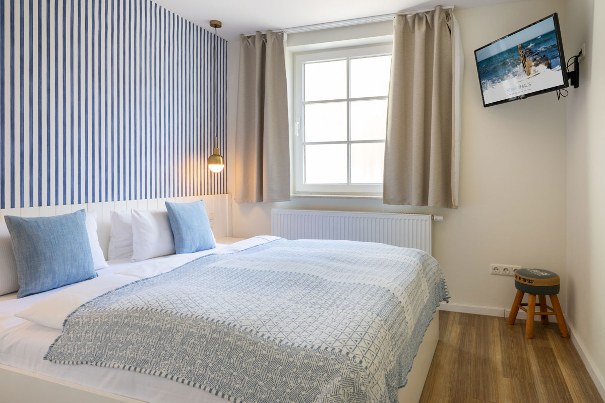 Schlafzimmer im Apartment des STRANDHAUS Ahrenshoop mit Doppelbett, blau-weißer Streifentapete und goldener Pendelleuchte.