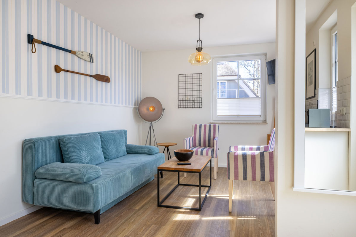 Wohnzimmer im Apartment des STRANDHAUS Ahrenshoop mit blauem Sofa, zwei Sesseln, Couchtisch und maritimem Wanddekor.