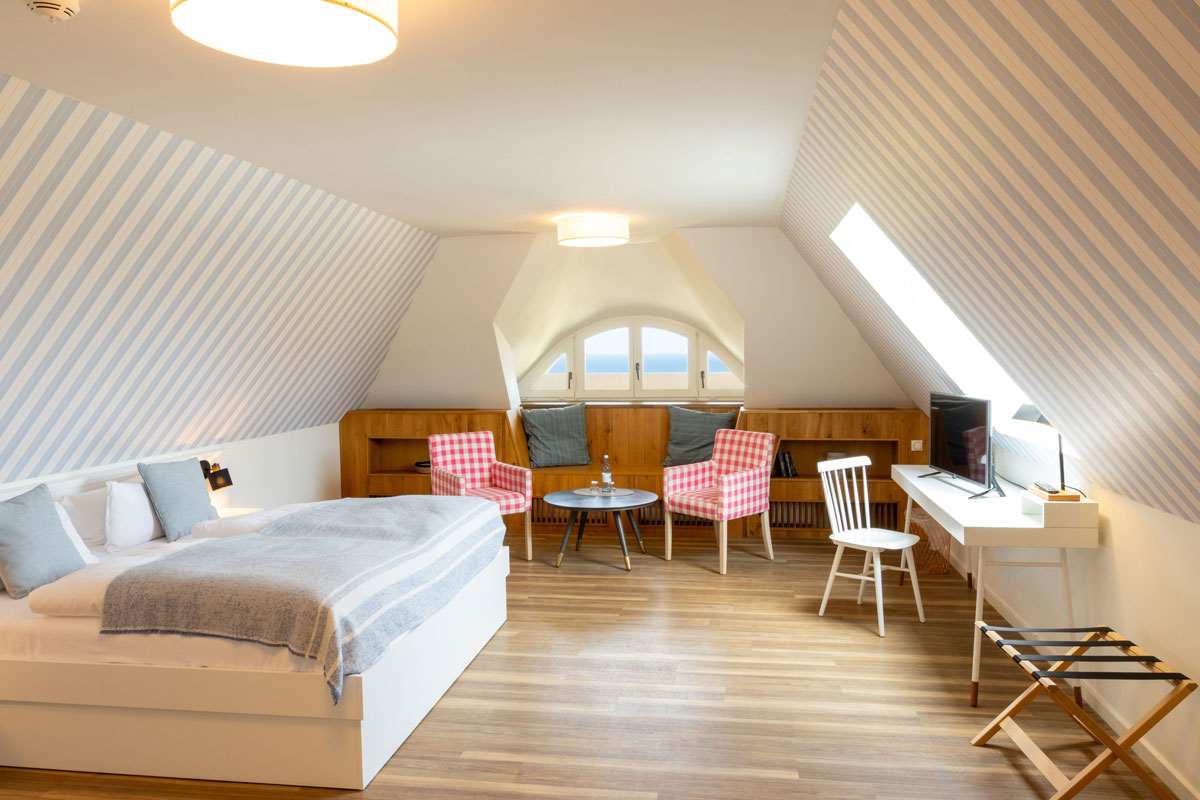 Gesamtansicht der Familiensuite im STRANDHAUS Ahrenshoop mit Doppelbett, Sitzecke, Schreibtisch und Meerblick durch das Rundbogenfenster.