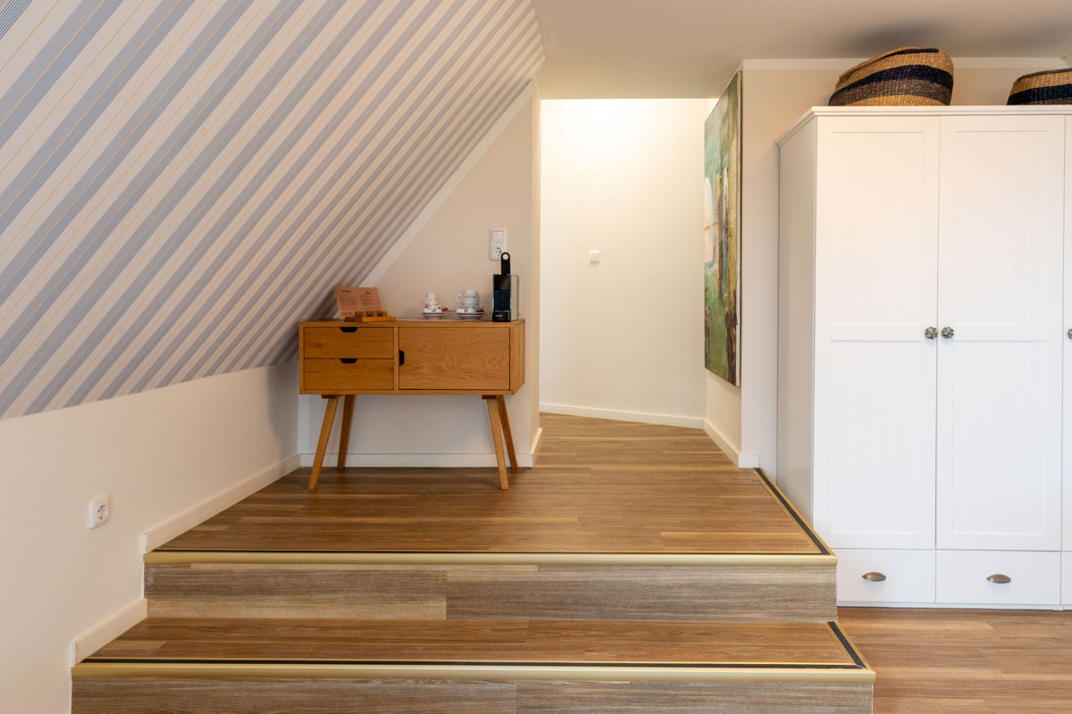 Flurbereich der Familiensuite im STRANDHAUS Ahrenshoop mit Holztreppe, Vintage-Kommode, Kaffeemaschine und weißem Kleiderschrank.