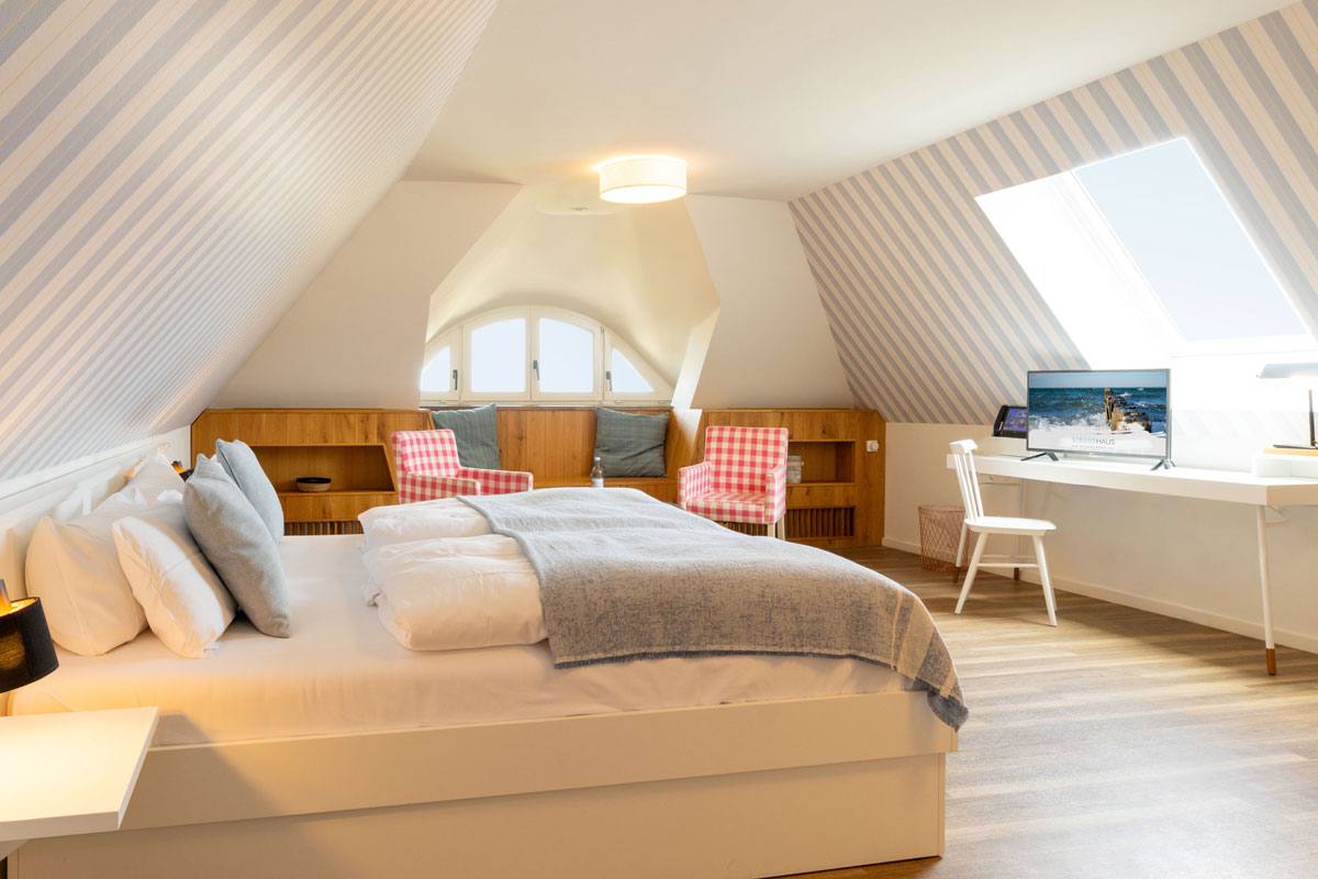 Familiensuite im STRANDHAUS Ahrenshoop mit Doppelbett, karierten Sesseln, Schreibtisch und Meerblick durch das Dachfenster.