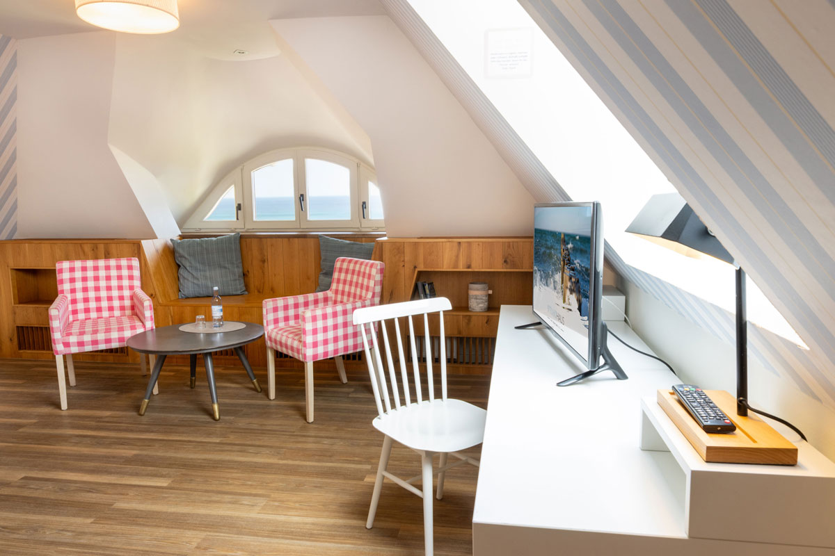 Wohnbereich der Familiensuite im STRANDHAUS Ahrenshoop mit zwei karierten Sesseln, Schreibtisch, TV und Meerblick.