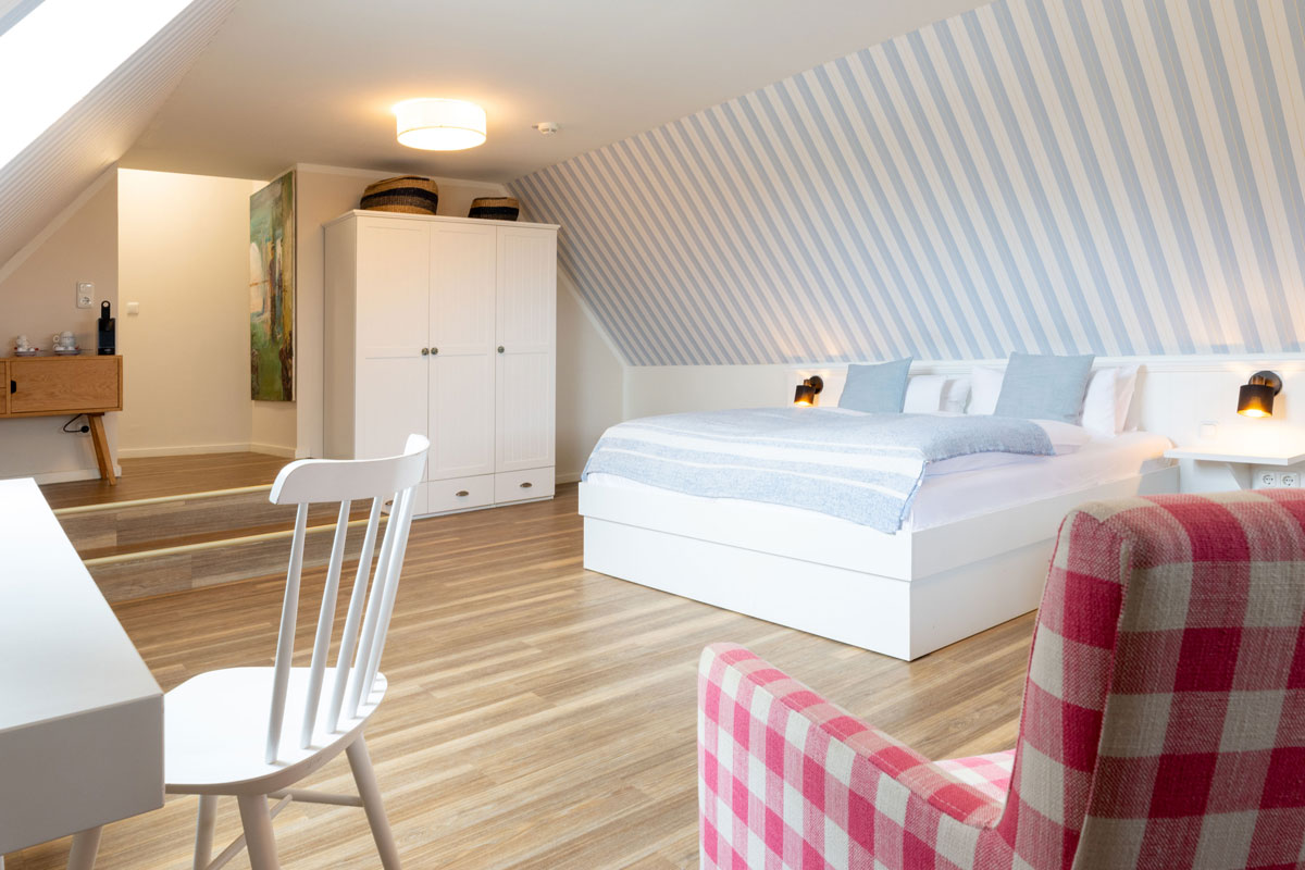 Familiensuite im STRANDHAUS Ahrenshoop mit Doppelbett, weißem Kleiderschrank, Schreibtisch und kariertem Sessel unter der Dachschräge.