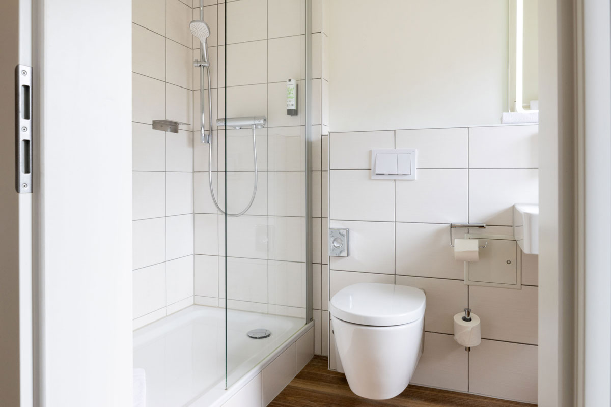 Bad im Familienzimmer des STRANDHAUS Ahrenshoop mit Glasdusche, WC und Waschbecken.