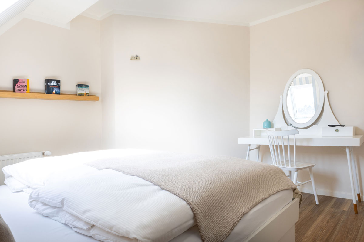 Schlafzimmer im Familienzimmer des STRANDHAUS Ahrenshoop mit Doppelbett, weißem Schminktisch, Spiegel und Bücherregal.