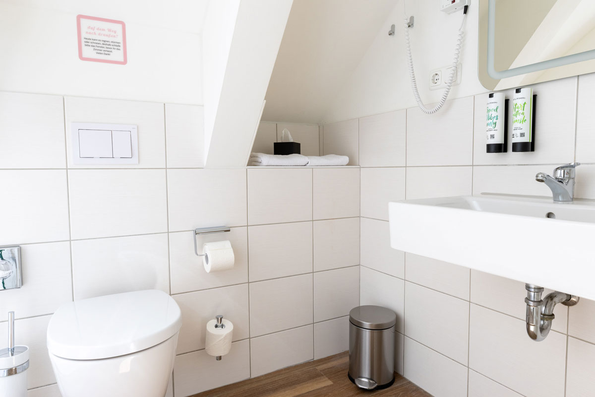 Bad im Dachzimmer Landseite des STRANDHAUS Ahrenshoop mit WC, Waschbecken, Spiegel und Dachschräge.
