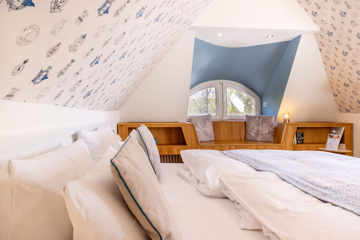 Blick vom Bett auf die Holzbank mit Rundbogenfenster im Dachzimmer Landseite des STRANDHAUS Ahrenshoop.