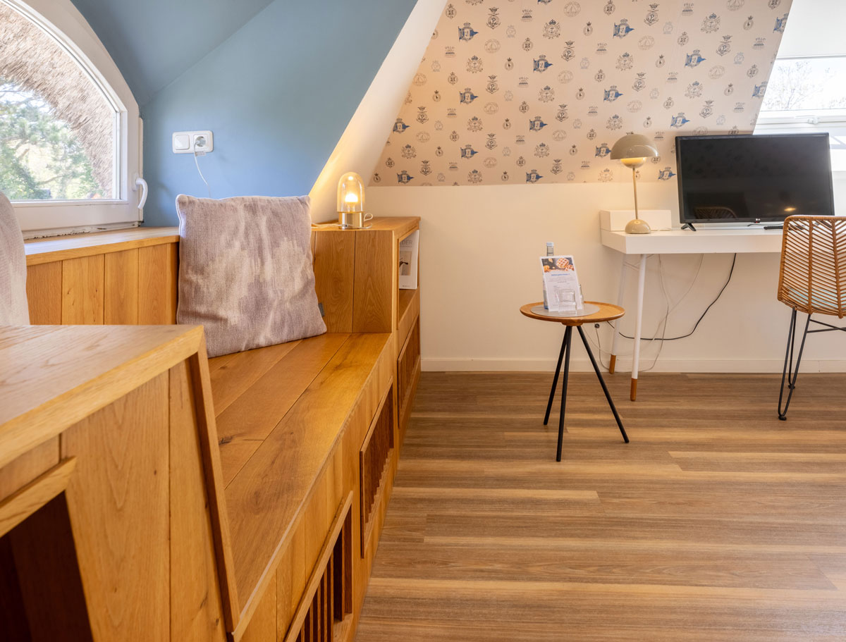 Sitzbereich im Dachzimmer Landseite des STRANDHAUS Ahrenshoop mit Holzbank, Schreibtisch, Rattanstuhl und maritimer Tapete.