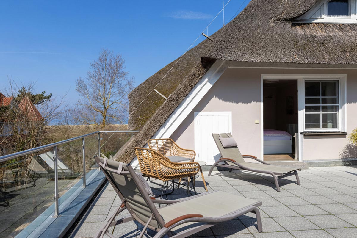 Sonnendeck des STRANDHAUS Ahrenshoop mit Liegestühlen, Rattanstuhl und direktem Zugang zum Zimmer unter dem Reetdach.