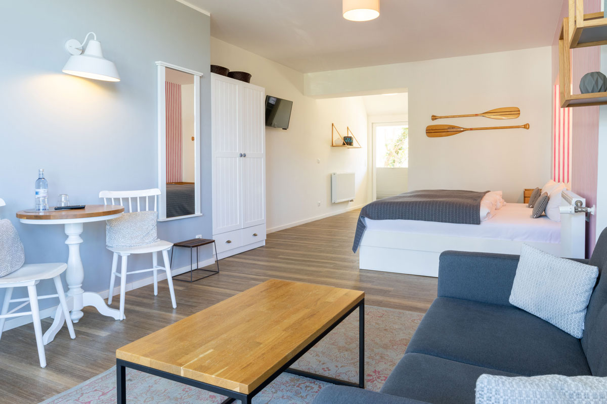 Geräumige Terrassensuite im STRANDHAUS Ahrenshoop mit Sofa, Esstisch, Doppelbett und maritimem Dekor.