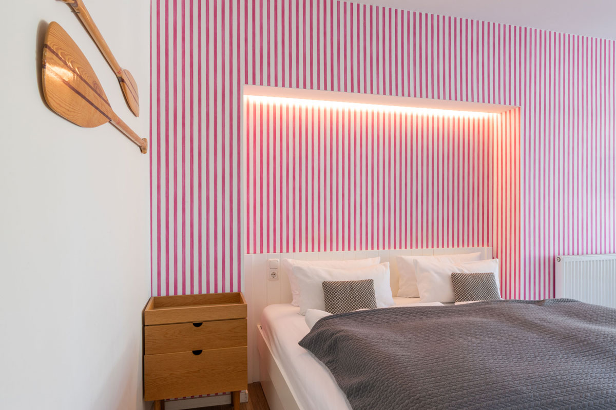 Schlafzimmer der Terrassensuite im STRANDHAUS Ahrenshoop mit Doppelbett, rot-weißer Streifentapete und maritimem Holzdekor.
