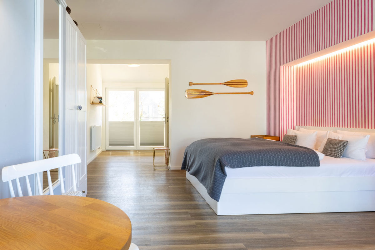 Geräumiger Schlafbereich der Terrassensuite im STRANDHAUS Ahrenshoop mit Doppelbett, Ruderdekor und Terrassentür.