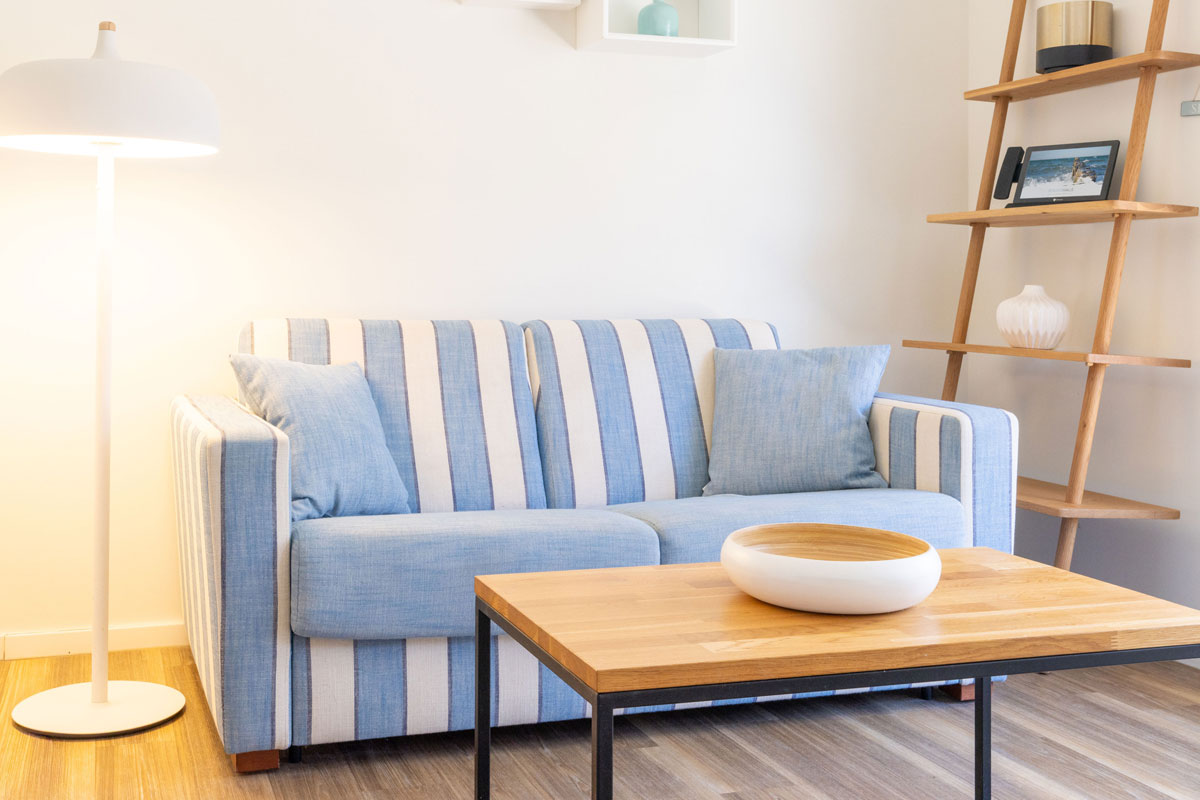 Sitzbereich der Terrassensuite im STRANDHAUS Ahrenshoop mit blau-weiß gestreiftem Sofa, Holzcouchtisch und Stehlampe.