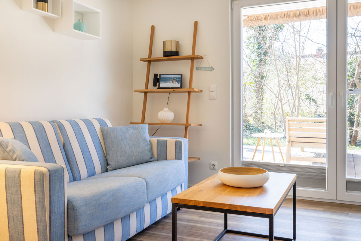 Wohnzimmer der Terrassensuite im STRANDHAUS Ahrenshoop mit blau-weißem Sofa, Couchtisch und direktem Blick auf die private Terrasse.
