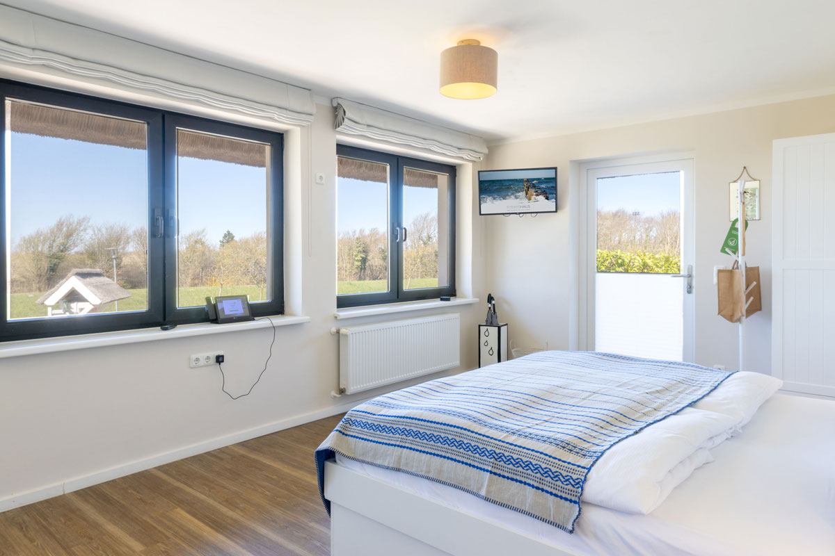 Helles Terrassenzimmer im STRANDHAUS Ahrenshoop mit Doppelbett, großen Fenstern mit Landschaftsblick und Terrassenzugang.