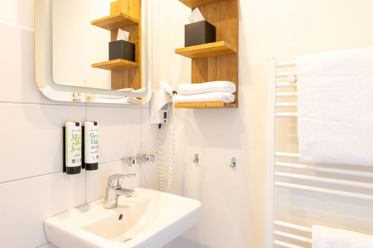 Badezimmer des Terrassenzimmers im STRANDHAUS Ahrenshoop mit Waschbecken, Holzregal, Handtüchern und Heizkörper.