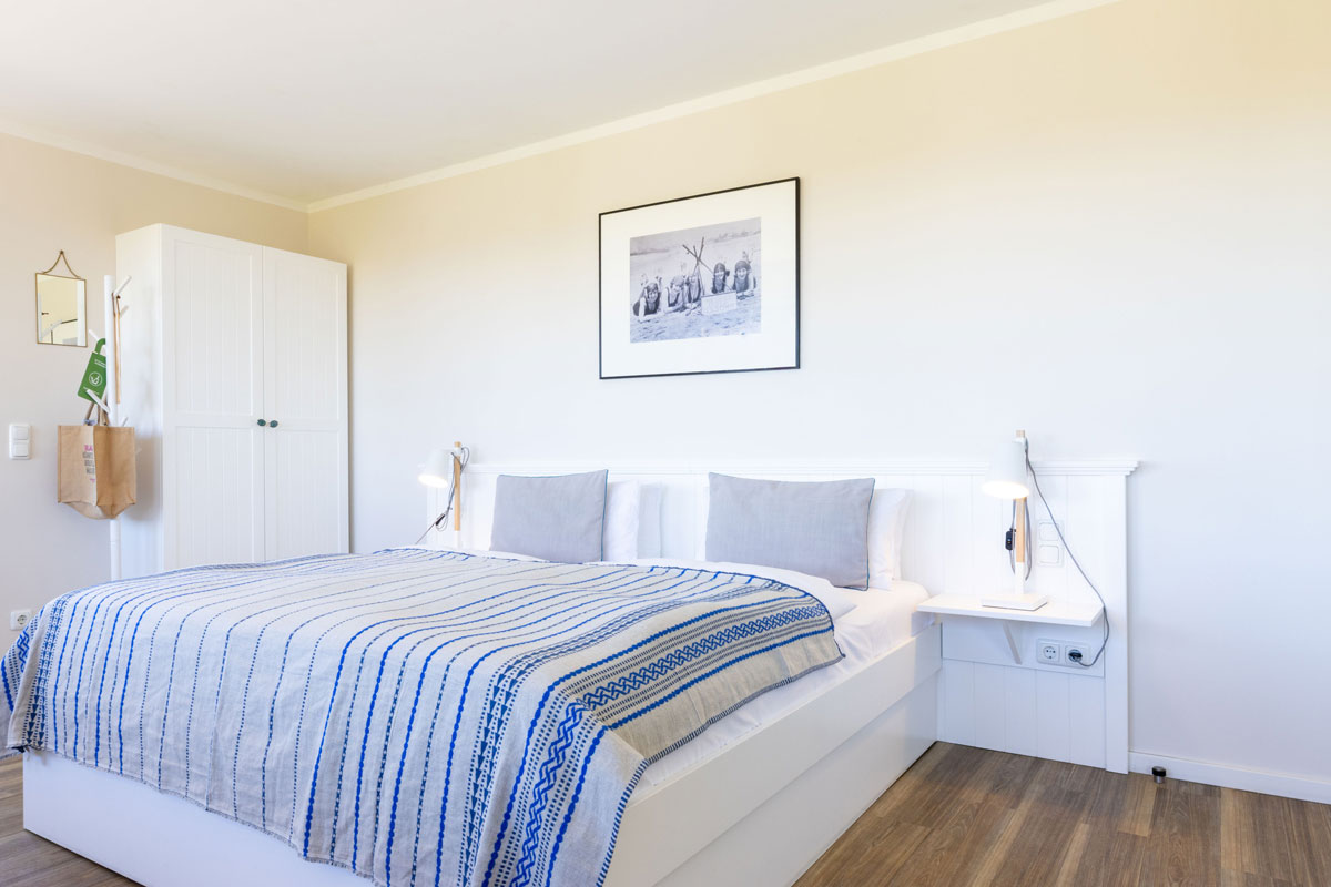 Helles Schlafzimmer des Terrassenzimmers im STRANDHAUS Ahrenshoop mit Doppelbett, weißem Kleiderschrank und Wandbild.